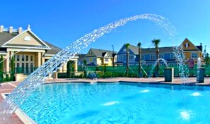A swimming pool with a water fountain feature, surrounded by residential houses.