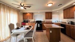 A modern kitchen with wooden cabinets, a central island, a dining area with a white table and chairs, and a ceiling fan. - Close strip 3 bedroom Home (Las Vegas,)