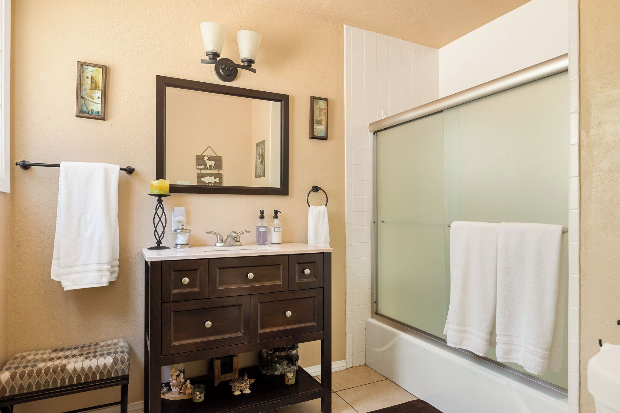 A bathroom with a dark wooden vanity, a mirror, a towel rack, a bench, and a glass-enclosed shower.