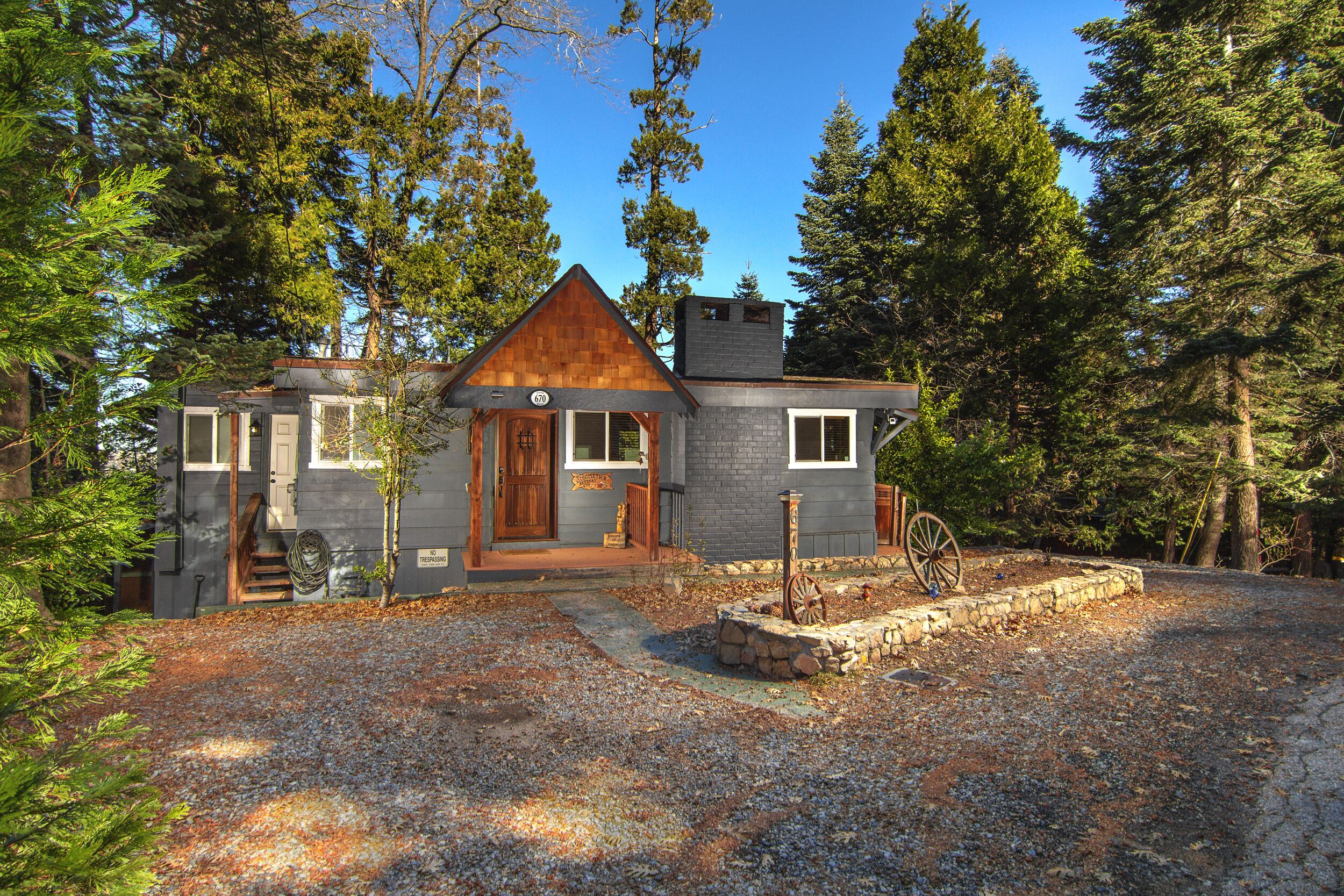 A rustic cabin with a wooden door, a stone foundation, and a gravel driveway.
