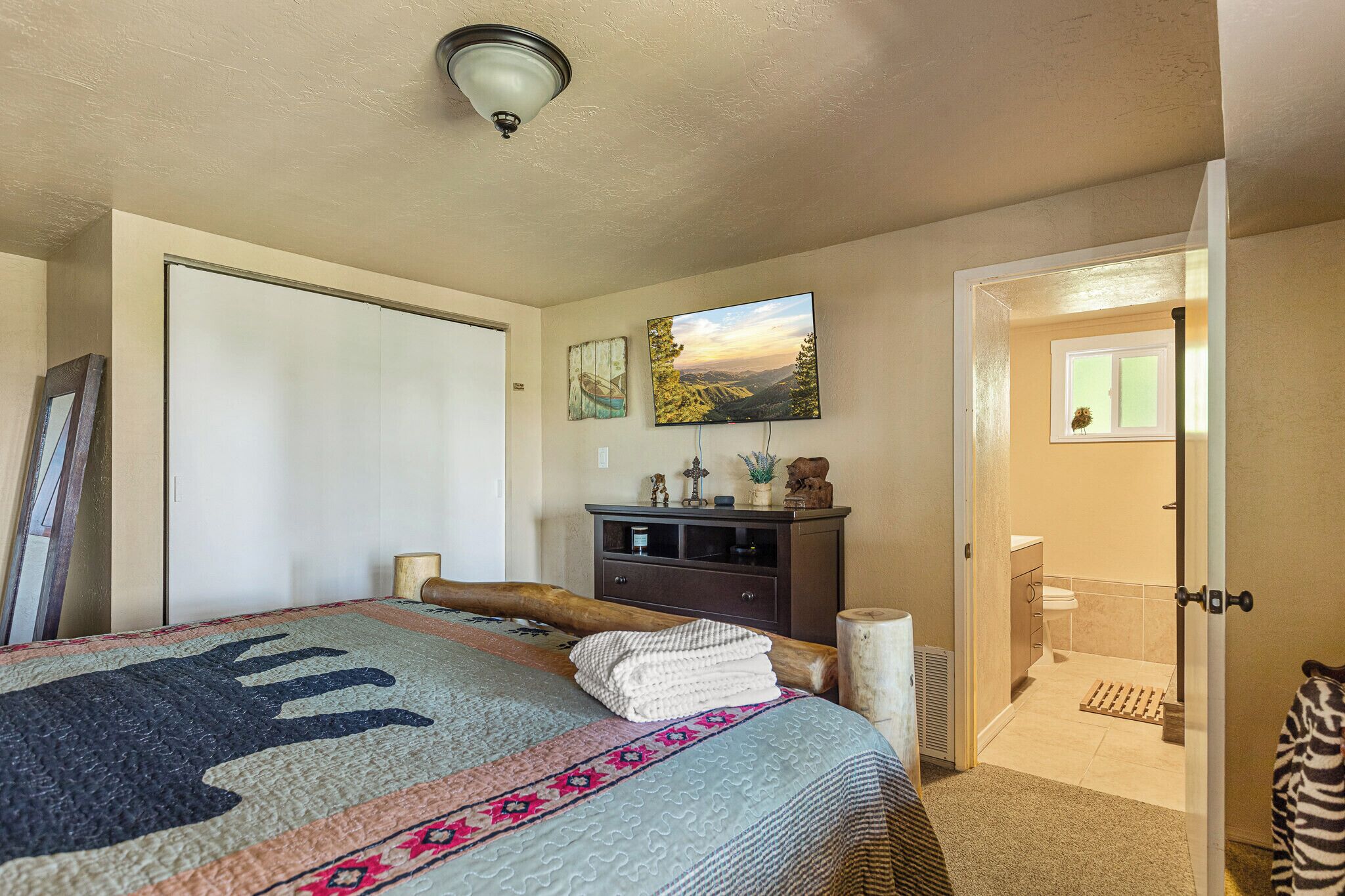 A bedroom with a bed, a dresser, a painting, and a bathroom visible through an open door.