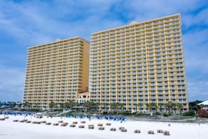 A high-rise hotel with multiple floors, a beach in the foreground, and a clear sky.