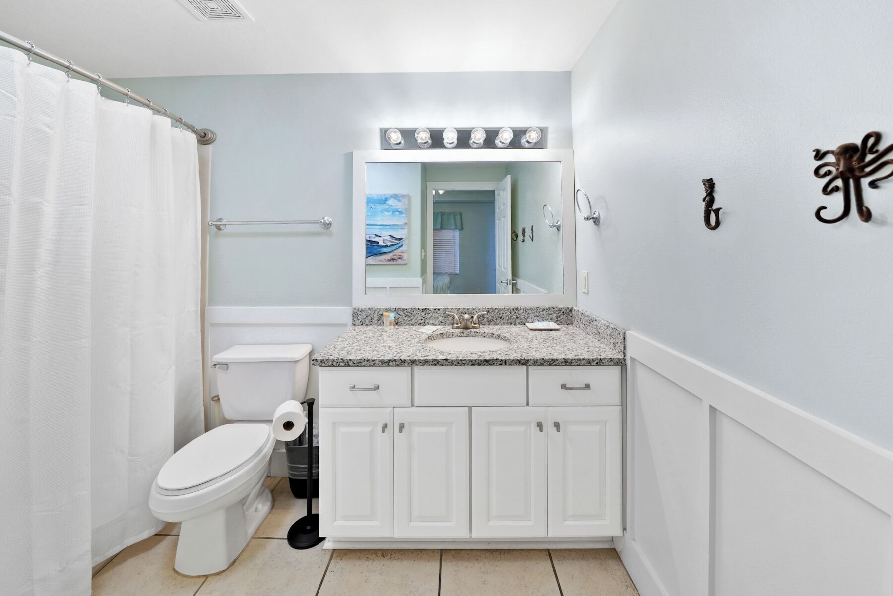 Une salle de bain équipée de toilettes, d’un lavabo, d’un miroir et d’un rideau de douche.