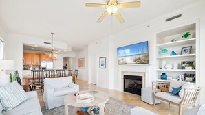 A spacious living room with a fireplace, white furniture, and a dining area with wooden chairs. - Adagio D405 Private Top 4th Floor Corner!! Premium Pool Front!+ Ice Maker! (Santa Rosa Beach)