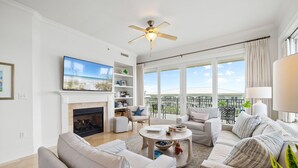 A spacious living room with a fireplace, comfortable seating, a flat-screen TV, and a balcony with a view. - Adagio D405 Private Top 4th Floor Corner!! Premium Pool Front!+ Ice Maker! (Santa Rosa Beach)