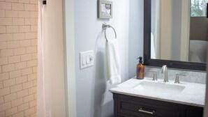 A bathroom with a white sink, dark cabinets, a towel rack, a framed picture, and a window.
