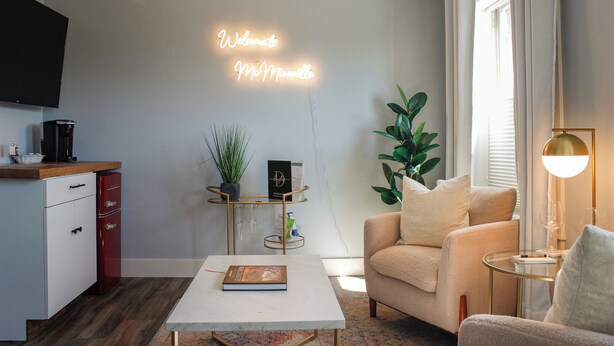 A modern living room with a white coffee table, a beige sofa, a glass coffee table, a red cabinet, a neon sign, and a potted plant.