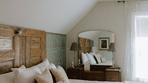 Une chambre avec un plafond en pente, une tête de lit en bois, un lit avec une literie blanche, une table de chevet avec une lampe et un miroir au-dessus du lit.