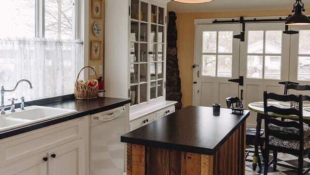 Une cuisine avec des meubles blancs, un carrelage noir et blanc et des luminaires suspendus.