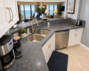 A modern kitchen with granite countertops, stainless steel appliances, a dishwasher, and a view of the ocean.