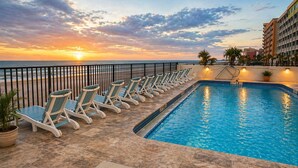 Un espace aménagé au bord de la piscine, avec des chaises longues et une vue sur le coucher de soleil sur l’océan.