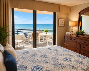 A hotel room with a balcony, a bed with a floral bedspread, a dresser, and a view of the ocean.