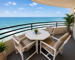 A balcony with a white table and chairs, a potted plant, and a view of the ocean.