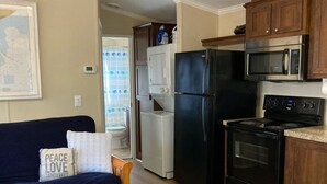 A compact kitchen with a refrigerator, microwave, and stove. There is a wooden dining table and a sofa with a cushion.