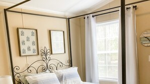 A four-poster bed with a white and gray striped bedspread, a bedside table with a lamp and books, and a wall clock.