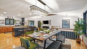 A spacious living area with a dining table set for six, a kitchen with wooden cabinets, and a large window providing natural light. - Big Pine Alpine | Pickleball, GameRoom, HotTub, EpicViews, Gym & More (Laurelville)
