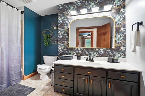 A bathroom with a dark blue wall, a white sink, and a large mirror with a leaf pattern.