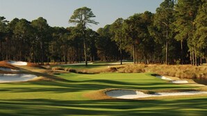 Ein Golfplatz mit Sandbunkern, Bäumen und blauem Himmel.