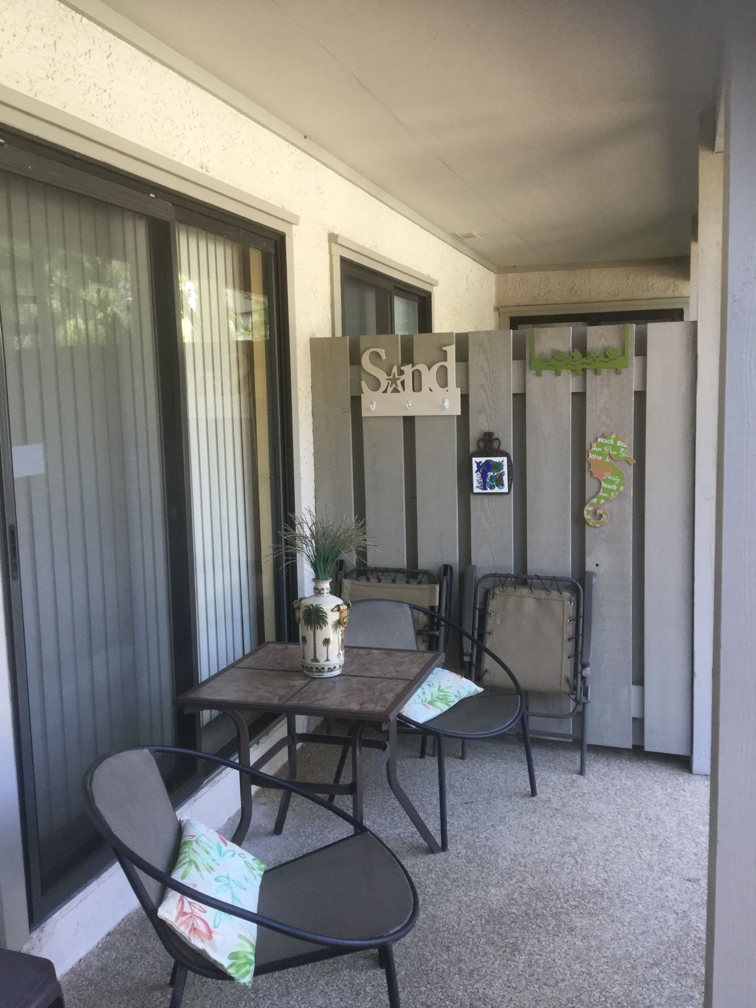 Un patio con una mesa, sillas, un letrero decorativo y una planta pequeña.