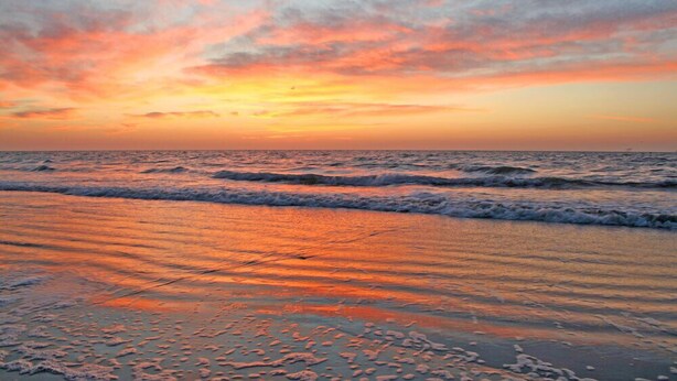 Ein Strand mit Wellen und einem Sonnenuntergang.