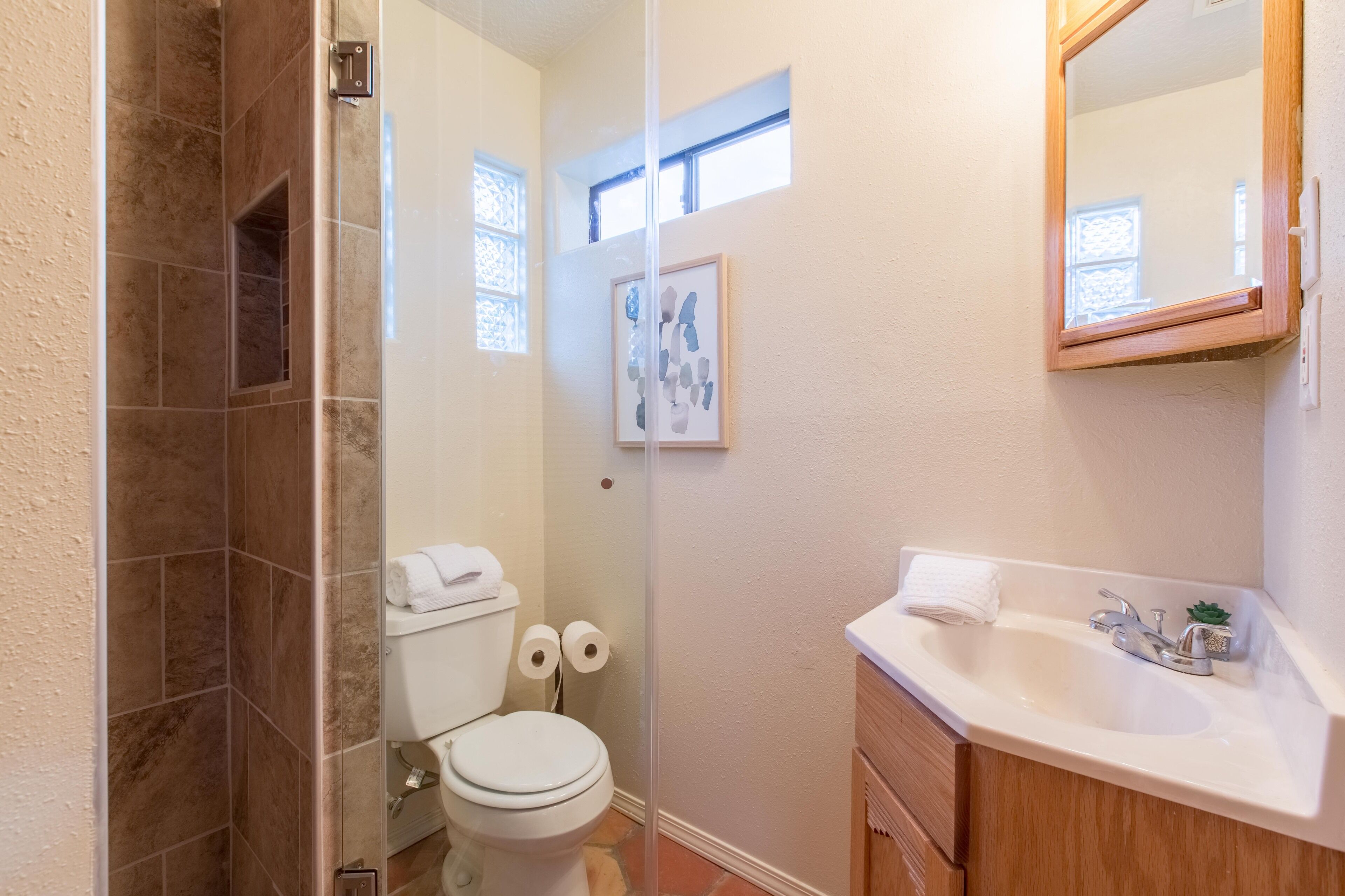 Une salle de bain équipée d’une douche, de toilettes, d’un lavabo et d’une œuvre d’art encadrée au mur.