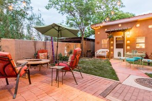 Een buitenpatio met tegels, metalen stoelen, een tafel en een parasol.
