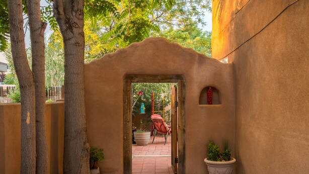 Un espace patio extérieur avec une porte donnant sur un jardin. On peut y voir des plantes en pot et une chaise rouge.