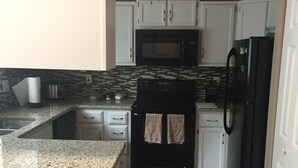 A kitchen with white cabinets, a black refrigerator, a microwave, a stove, and a ceiling fan. - Charming home in Mountain Shadows. (Colorado Springs)