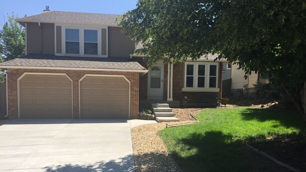 A two-story house with a large garage, a well-maintained lawn, and a tree providing shade. - Charming home in Mountain Shadows. (Colorado Springs)