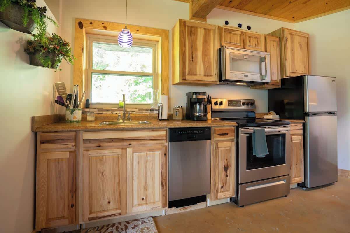 A kitchen with wooden cabinets, a dishwasher, a stove, a refrigerator, and a window with plants on the wall.