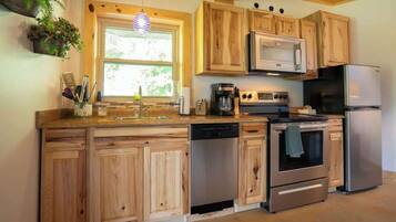 A kitchen with wooden cabinets, a dishwasher, a stove, a refrigerator, and a window with plants on the wall.