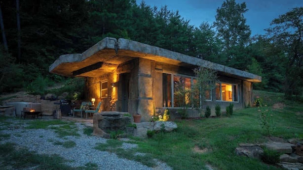Un chalet rustique avec une façade en pierre, un foyer extérieur, des sièges de jardin et un jardin bien entretenu.