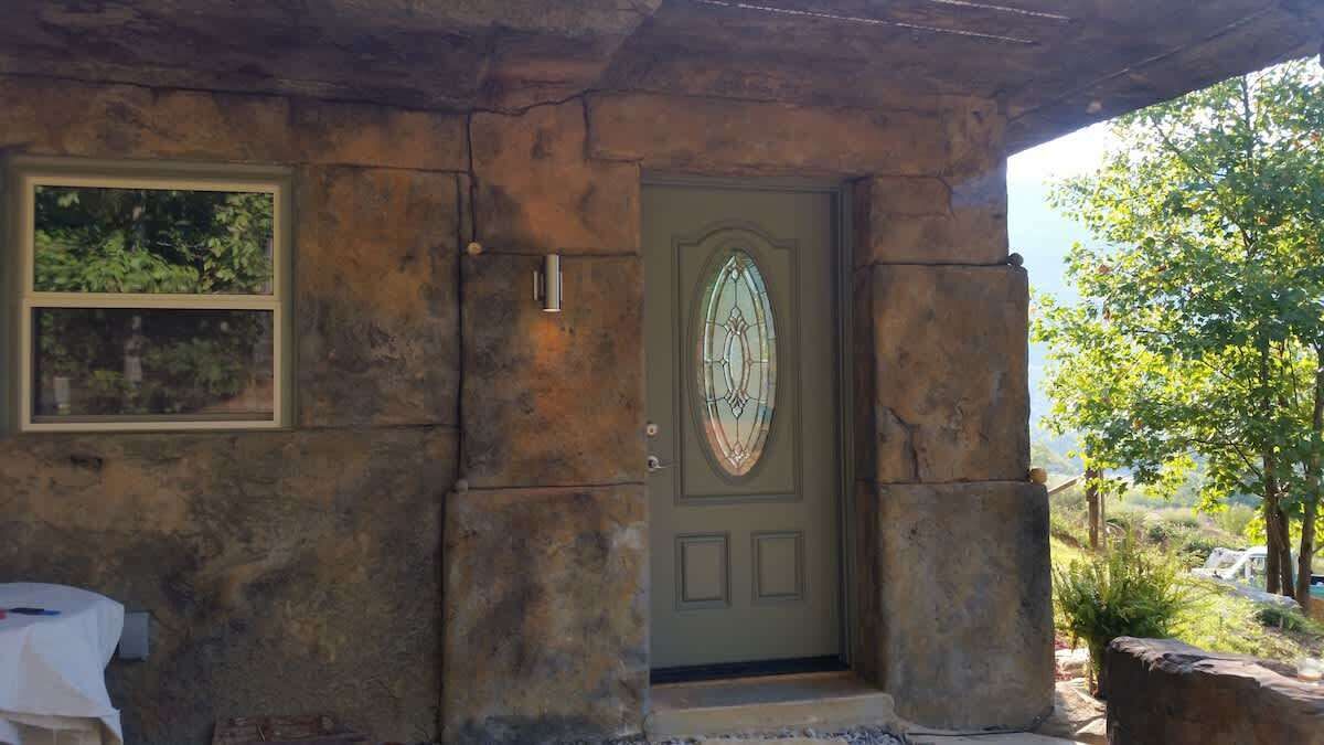 A stone building with a green door, a window, and a stone bench.