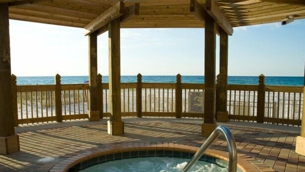 Un belvédère en bois avec un jacuzzi, donnant sur une plage.
