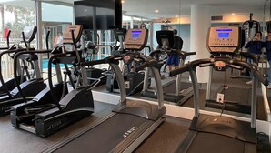 Une salle de sport équipée de plusieurs tapis de course, de vélos d’exercice et d’un grand miroir.