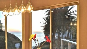 Ein Zimmer mit Holztisch, Blumen in einer Vase und Blick auf den Ozean durch große Fenster.