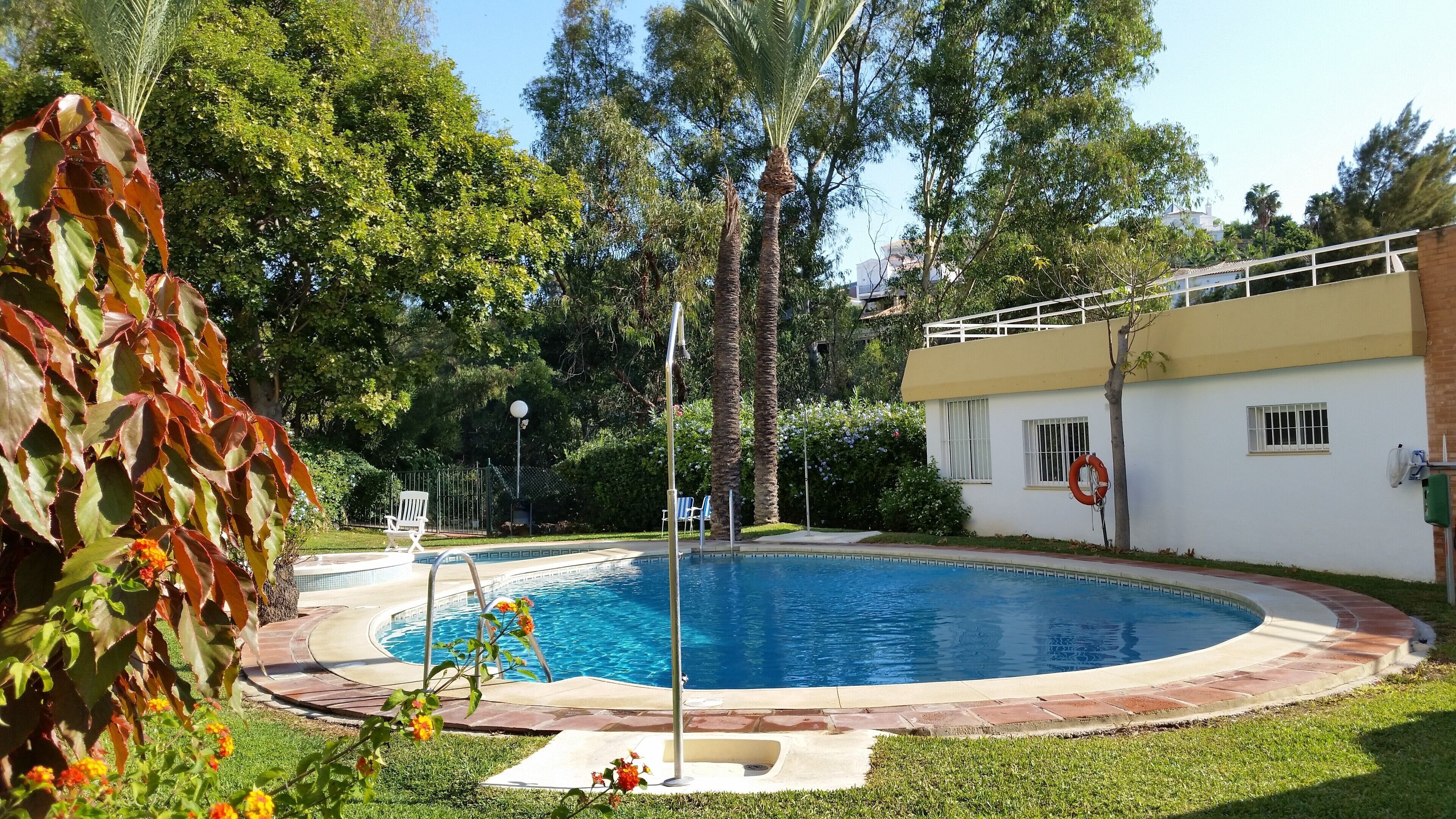Ein Swimmingpool mit umlaufender Terrasse, einem Rettungsring und einem weißen Gebäude mit vergitterten Fenstern.