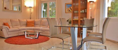 A modern living room with a glass coffee table, beige sofa, and matching chairs.