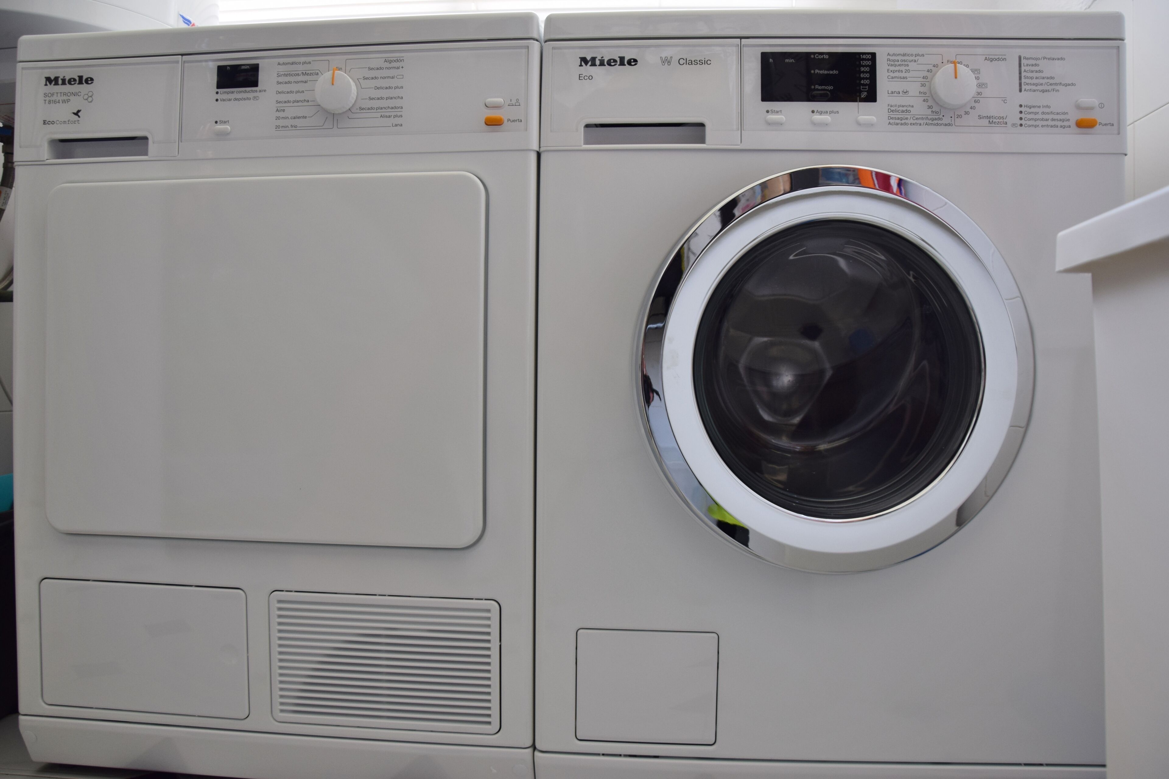 Eine weiße Miele Waschmaschine mit Bedienfeld, einer Frontlader-Türe und einem Lüftungsschlitz unten.