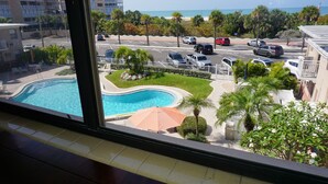 A view of a swimming pool surrounded by a landscaped area with palm trees and a parking lot in the background. - Gulf views! 2 Bedroom vintage condo - Third/Top Floor. FN #205 (St Pete Beach)