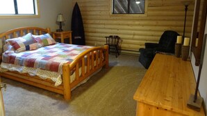 A log cabin room with a wooden bed, a small table, a chair, and a ceiling fan.