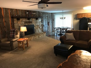 Una sala de estar acogedora con chimenea de piedra, ventilador de techo y comedor con mesa y sillas.