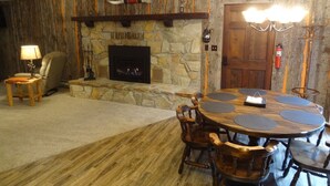 A cozy living room with a stone fireplace, wooden dining table, and chairs.