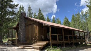 A rustic cabin with a stone chimney, wooden deck, and a gravel driveway.