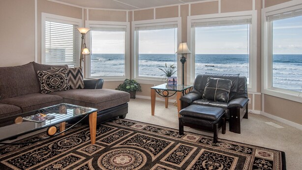 A living room with a view of the ocean, a leather sofa, a glass coffee table, and a patterned rug.