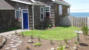 A two-story house with a blue door, stone siding, and a small front yard with a stone pathway and plants.