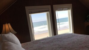 A room with a bed, a lamp, and a view of the beach through a window.