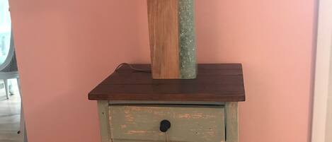 A wooden nightstand with a lamp, two wicker baskets, and a pink wall.