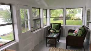 A sunroom with large windows, wicker furniture, and a patterned rug. - Charming lake front cabin on Highland Lake (Andover)