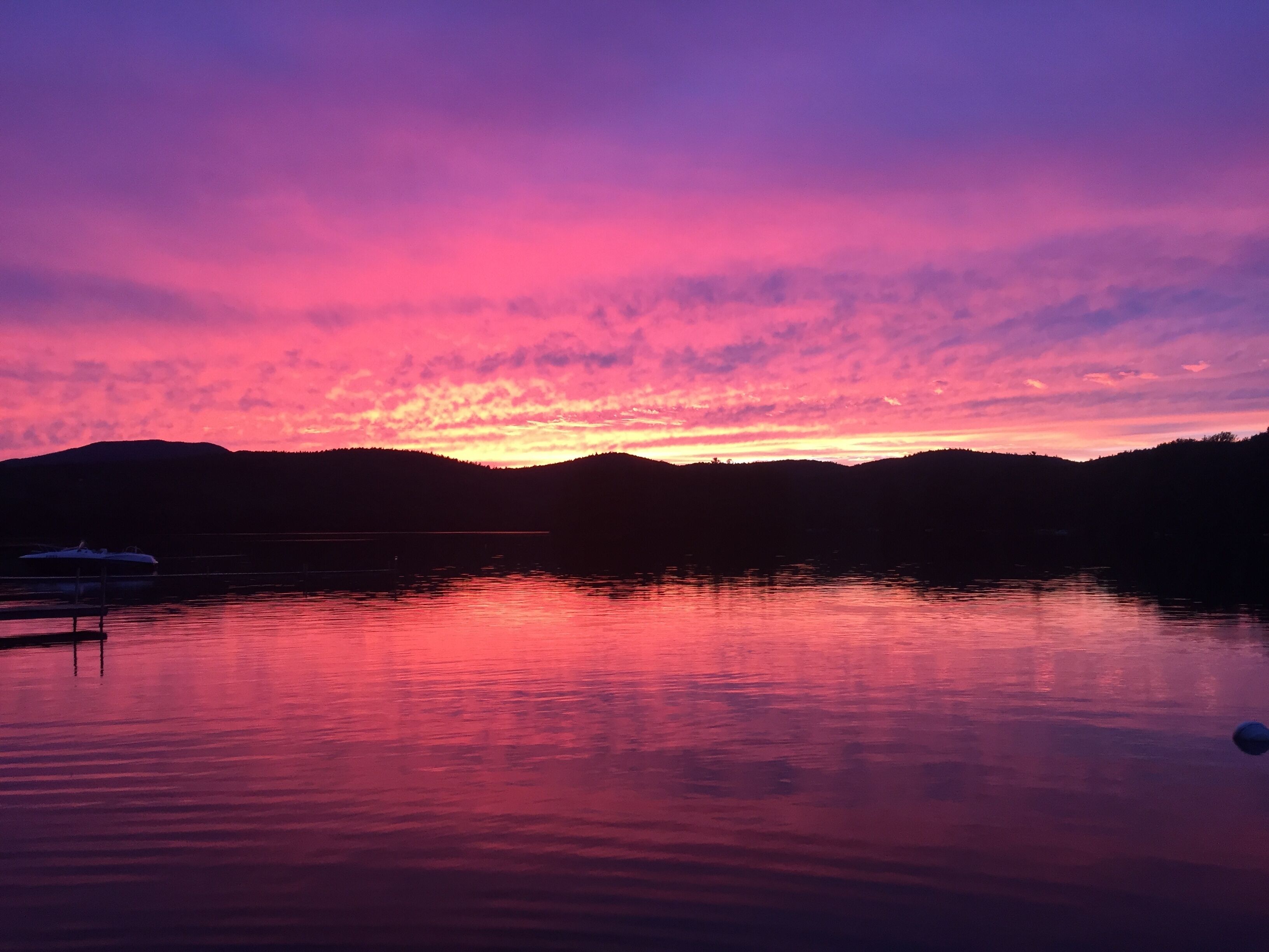 Een rustig meer bij zonsondergang met een steiger en een boot.